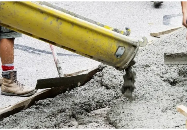 Betoniarka wylewa świeży beton. Pracownicy przygotowują teren, a pytanie "jak długo podlewać beton" jest kluczowe dla jego trwałości.