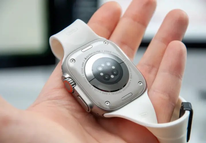Naprawa smartwatcha Apple Watch Ultra. Widok na tył zegarka z białym paskiem, trzymanego w dłoni.