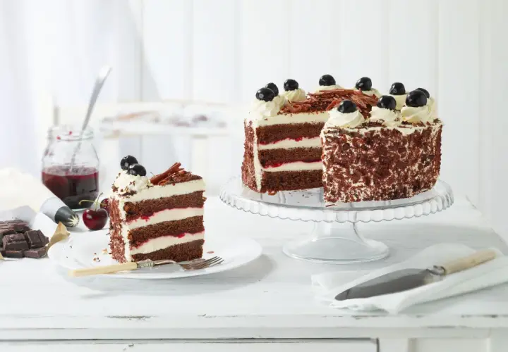 Una fetta di foresta nera torta, con strati di cioccolato, panna e ciliegie, accanto a una torta intera decorata.