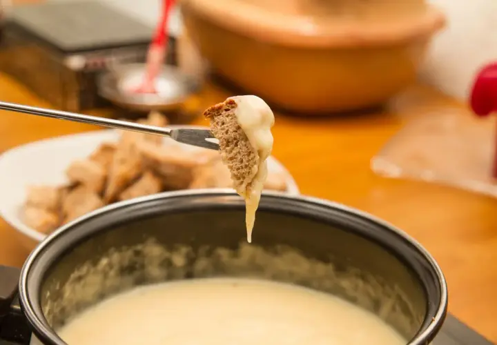 Un morceau de pain trempé dans une fondue savoyarde sans appareil. Le fromage dégouline sur la fourchette.