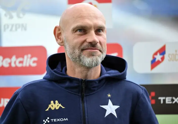 Łysy mężczyzna z siwą brodą, trener Wisły Kraków, w granatowej bluzie z kapturem z logo klubu.