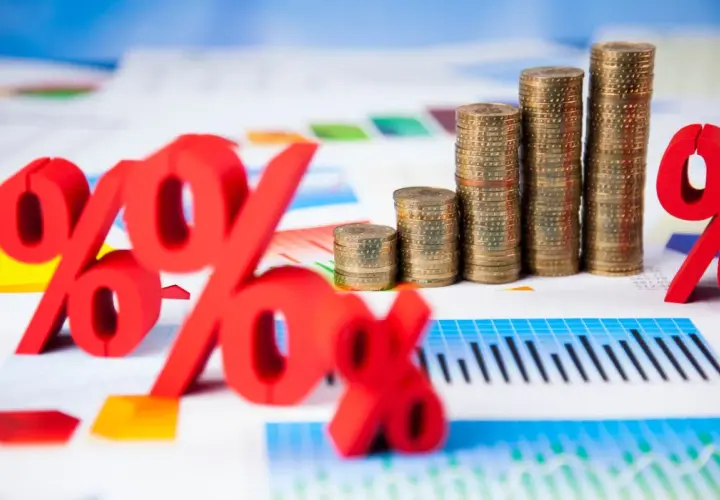 Rote Prozentzeichen und Münzstapel auf Finanzdiagrammen. Sie fragen sich, was sind Zinsen? Hier sehen Sie die Antwort visuell dargestellt.