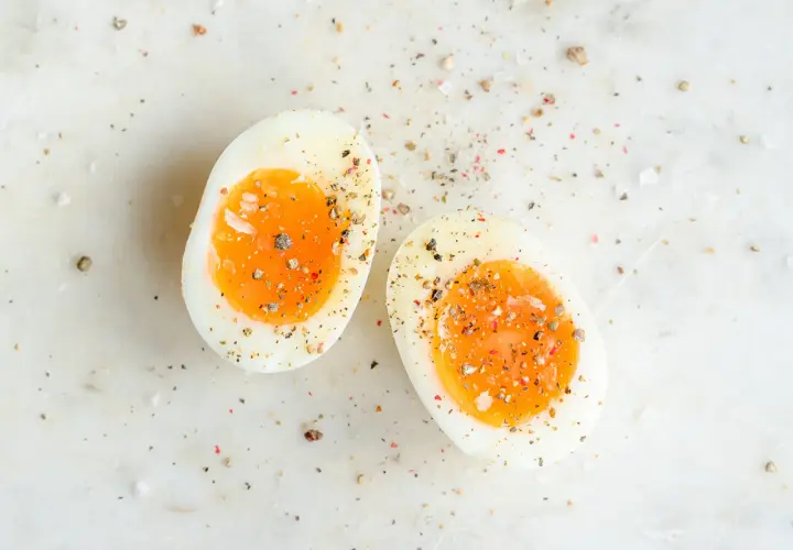 Deux moitiés d'oeuf dur trop cuit, saupoudrées de sel et de poivre, sur une surface marbrée.