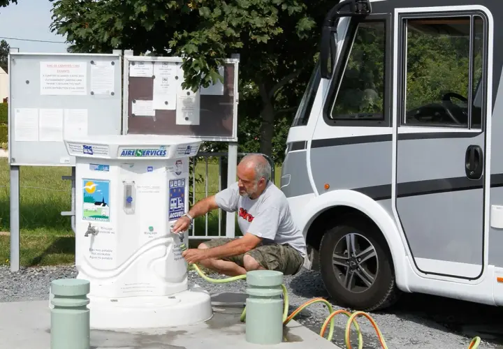 Un homme remplit un tuyau à un point d'eau pour camping-car. L'aire de services propose de l'eau potable et non potable.