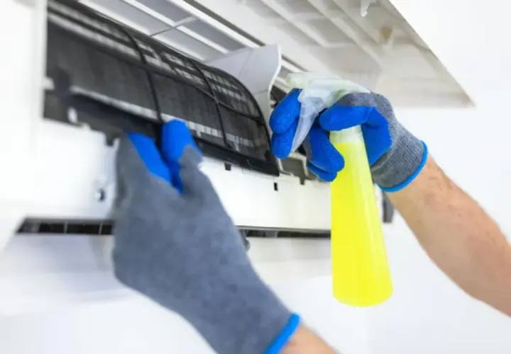 Manos enguantadas sacan filtro de aire acondicionado para limpiarlo con spray.