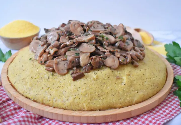Polenta z duszonymi pieczarkami na drewnianej desce, obok miseczka mąki kukurydzianej.