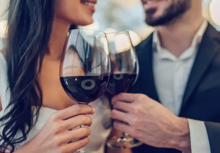 Ein Paar hebt Gläser mit Rotwein zum Anstoßen. Ein Glas Rotwein kann gesund sein, wenn er in Maßen genossen wird.