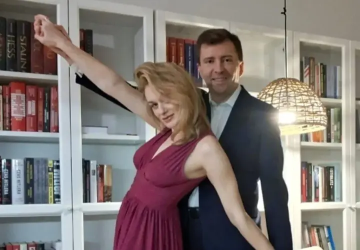Łukasz Schreiber z żoną pozują na tle regałów z książkami. Ona w błyszczącej sukni, on w garniturze.