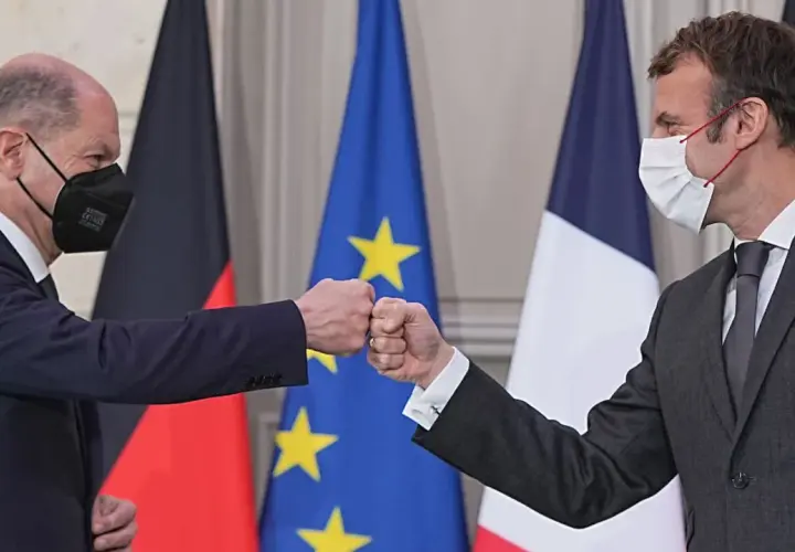 Olaf Scholz und Emmanuel Macron stoßen Fäuste vor den Flaggen von Deutschland und Frankreich.