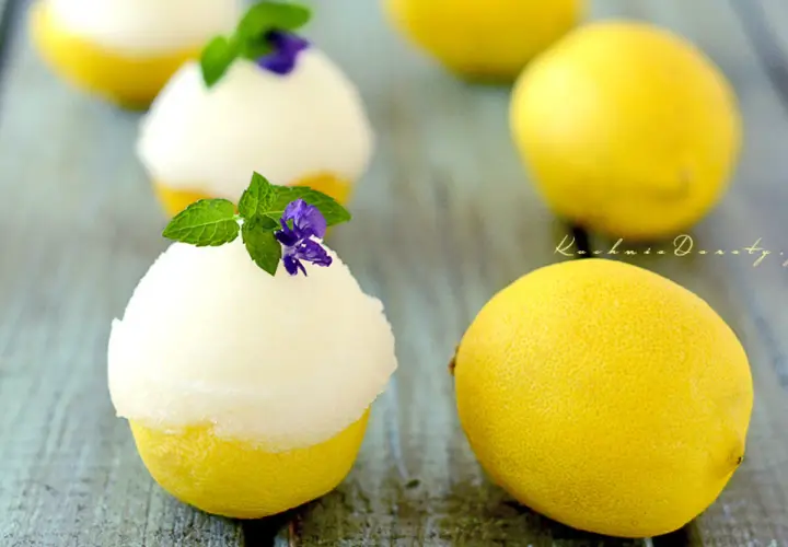 Orzeźwiający sorbet cytrynowy podany w wydrążonych cytrynach, udekorowany miętą i fioletowym kwiatkiem.