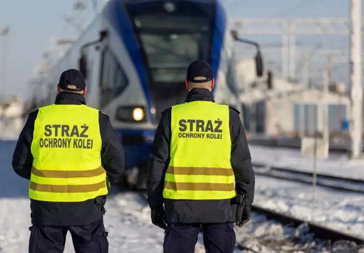 Dwóch funkcjonariuszy Straży Ochrony Kolei w kamizelkach odblaskowych stoi przed pociągiem. Czy mogą wystawić mandat?