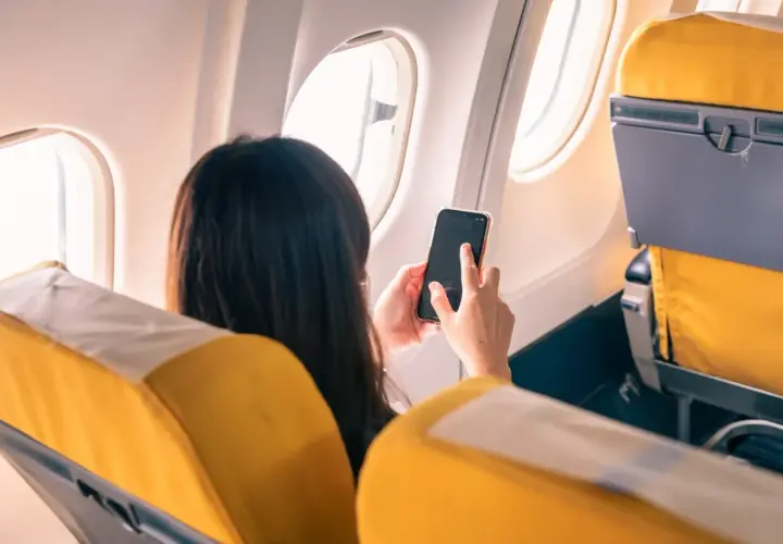 Kobieta w samolocie korzysta z telefonu, pamiętając o włączeniu trybu samolotowego.