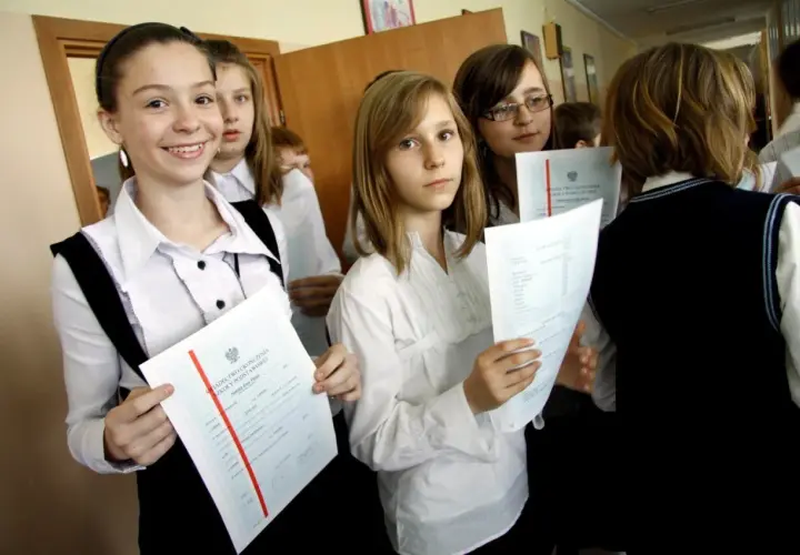 Uczennice z dyplomami, jedna z nich uśmiecha się, zastanawiając się, jaka średnia na czerwony pasek w 4 klasie.