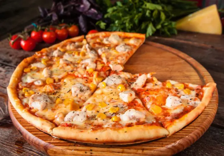 Pyszna pizza z kurczakiem i kukurydzą, podana na drewnianej desce, z pomidorkami koktajlowymi i bazylią w tle.
