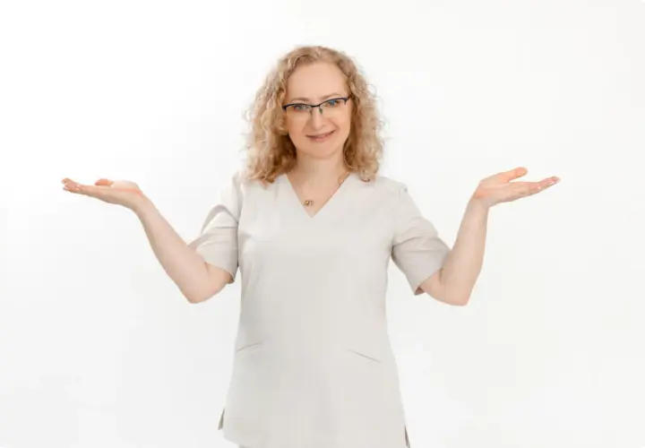 Kobieta w okularach i jasnym uniformie medycznym z otwartymi dłońmi.