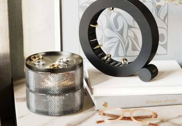 Un joyero vertical circular negro exhibe anillos dorados. A su lado, un joyero cilíndrico plateado con dos niveles.