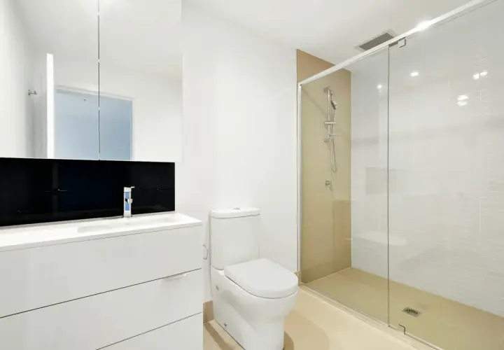 Mampara de ducha de cristal con medidas adecuadas para que no salga el agua. Baño moderno con lavabo, inodoro y ducha.