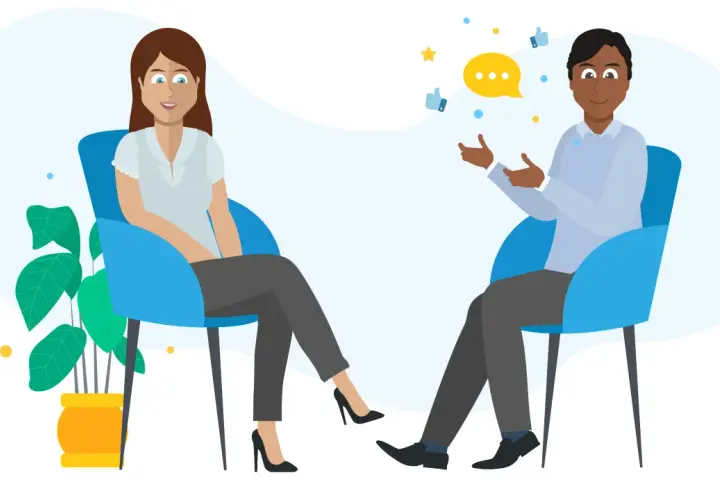 A man and woman sit in chairs, discussing. A speech bubble and thumbs-up icons suggest they are learning how to give feedback effectively.