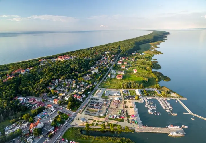Widok z lotu ptaka na Krynicę Morską. Widać zalew, lasy, zabudowania i tętniący życiem rynek z mariną pełną łodzi.