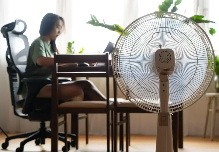 Kobieta pracuje przy biurku, a obok stoi wentylator pokojowy. Zastanawiasz się, ile prądu zużywa wentylator pokojowy?