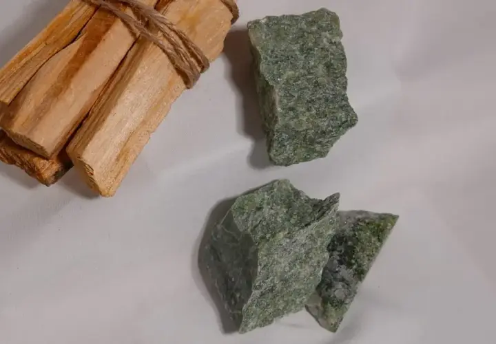 Surowe kawałki zielonego jadeitu, kamienia o cenionych właściwościach, leżą obok wiązki drewna Palo Santo.