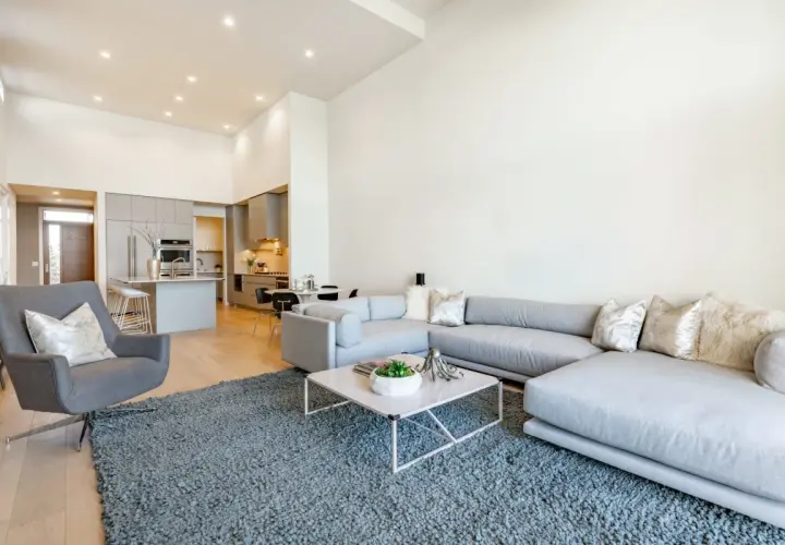Nowoczesny salon z szarą sofą i fotelem, otwartą kuchnią i jadalnią. Idealne wnętrze do życia, jak w ofercie Vinci Immobilier Polska.