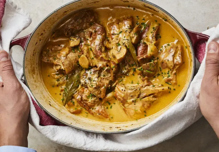 Un plat de lapin à la moutarde crémeuse, garni de persil frais et de champignons, servi dans une cocotte en fonte.
