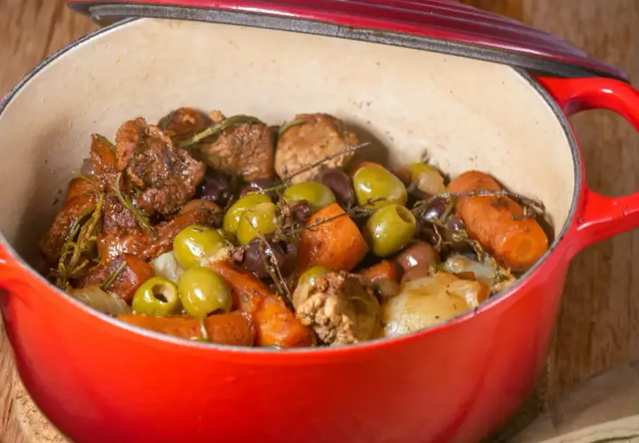 Un savoureux sauté de veau aux olives, carottes et herbes aromatiques mijote dans une cocotte rouge.