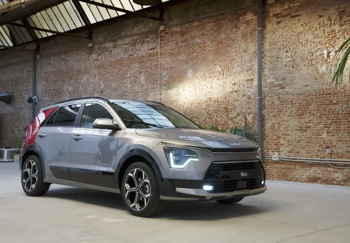 Un Kia Niro gris con detalles rojos en el pilar C, listo para una prueba. El coche está en un interior con paredes de ladrillo y techo acristalado.