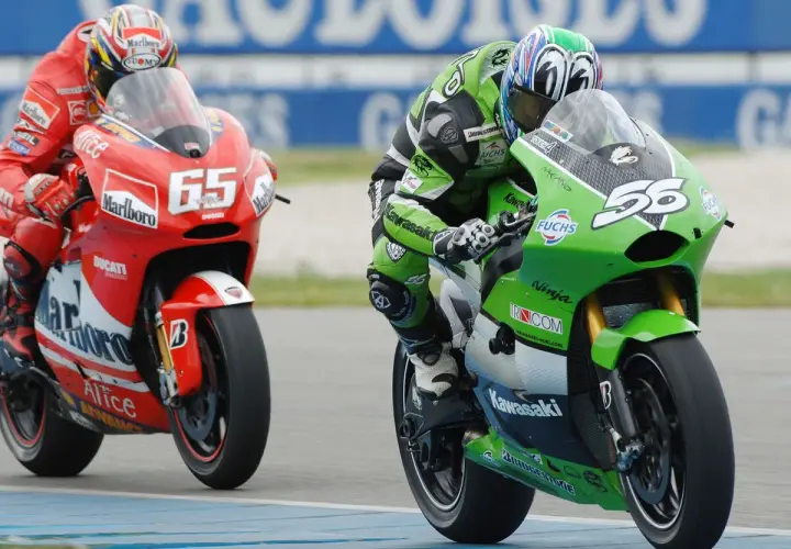 Piloto en moto verde Kawasaki compite en MotoGP, con el número 56. A su lado, otro piloto en rojo Ducati con el 65.