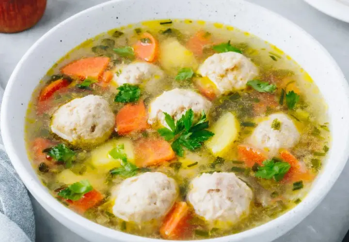 Zupa klopsowa babci: aromatyczny bulion z klopsikami, ziemniakami i marchewką, posypana natką pietruszki.