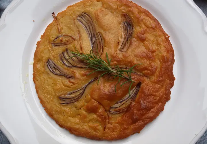 Herzhafte Kichererbsenmehl Rezepte: Goldbrauner Kuchen mit roten Zwiebeln und Rosmarin auf weißem Teller.
