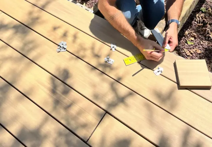 Pose d'une lame composite sur plot. Un artisan mesure avec une règle et un crayon pour une installation précise.