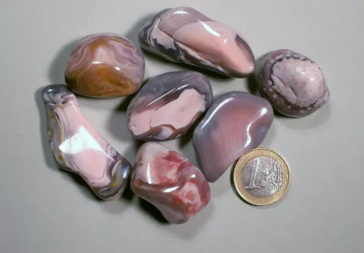 Glatt geschliffene Botswana Achat Steine in Rosa-, Grau- und Brauntönen, daneben eine 1-Euro-Münze.