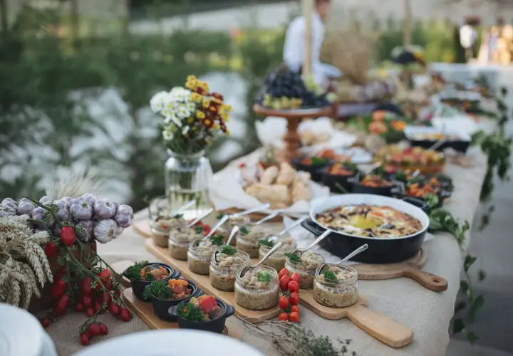Un buffet baptême chic en extérieur, avec des verrines, des plats chauds et des décorations naturelles comme de l'ail et des tomates.