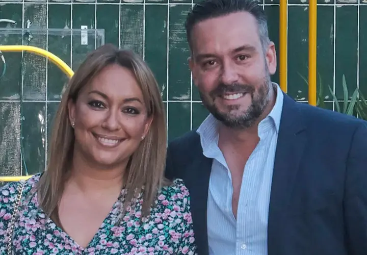 Kike Calleja y su pareja sonríen a la cámara. Ella lleva un vestido floral y él un traje azul.