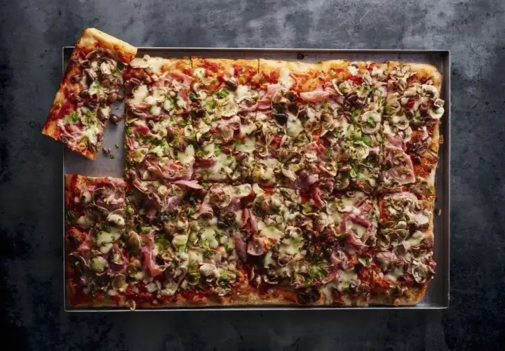 Pyszna pizza domowa na blachę z szynką, pieczarkami i oliwkami. Idealna na rodzinne spotkanie, przepis na blachę sprawia, że jest łatwa do przygotowania.