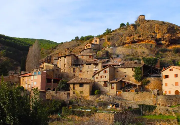 Un pintoresco senet de Barrabés se aferra a la ladera, con casas de piedra y tejados de teja bajo un cielo azul.