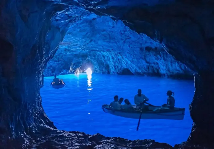 Barche a remi navigano nelle magiche grotte blu, illuminate da una luce surreale che rende l'acqua di un blu intenso.