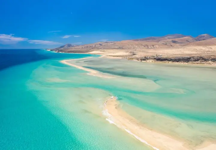 Aguas turquesas y arena dorada en Fuerteventura. Un paraíso natural para descubrir qué ver en Fuerteventura, con montañas áridas al fondo.