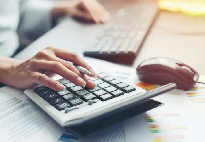 Dłoń z długopisem naciska klawisze kalkulatora, obok klawiatura i myszka. Analiza finansowa dla BNP Paribas Leasing.