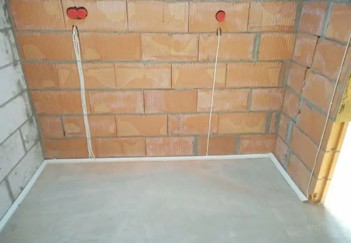 Przewody w posadzce bez peszla, przygotowane do dalszych prac instalacyjnych. Widoczne puszki instalacyjne w ścianie z cegły.