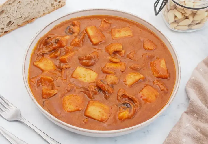 Un plato humeante de jibia en salsa, con trozos de patata y pan rústico al lado.