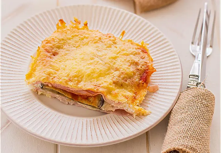 Porción de pastel de berenjenas gratinado con queso dorado, servido en plato blanco.