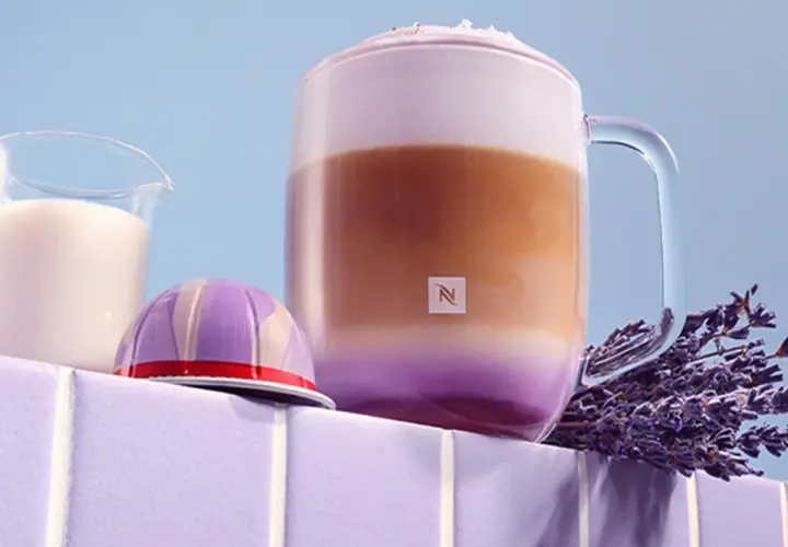 Ein aromatischer Lavendel Latte in einem Glasbecher, daneben eine Kaffeekapsel und Milch.