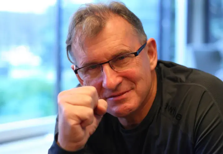 Jerzy Górski w okularach, opierający pięść o policzek, uśmiecha się.