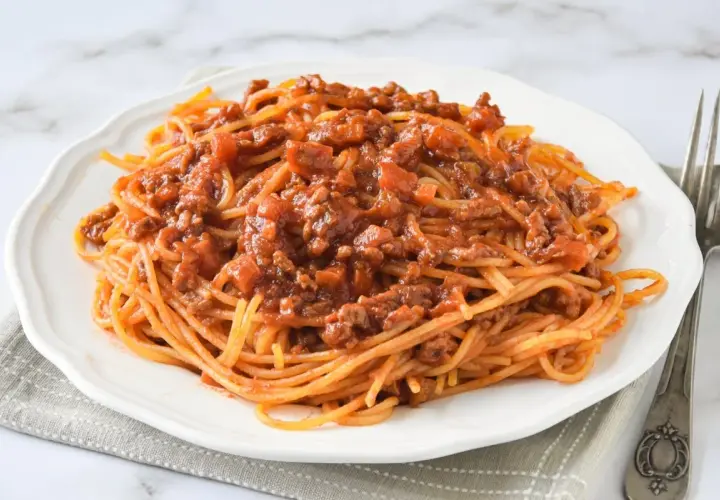 Un plato de espaguetis con carne picada, cubierto con una rica salsa de tomate y trozos de carne.