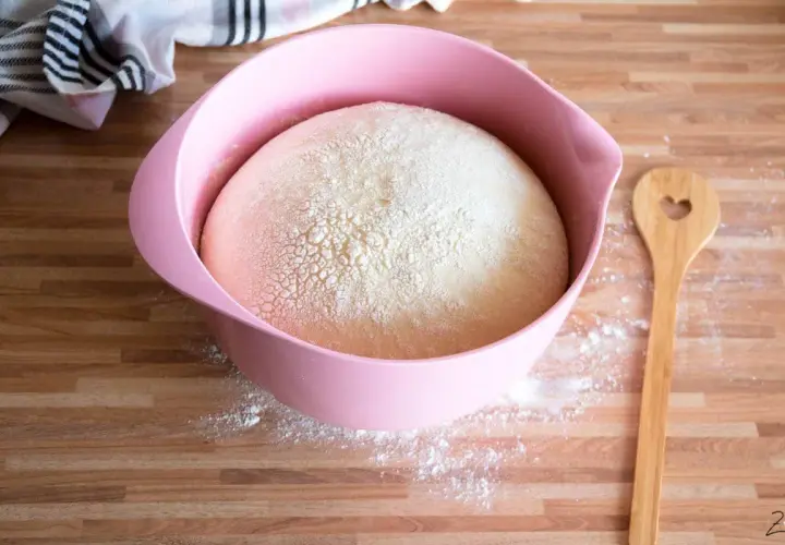 Hefeteig in rosa Schüssel, bereit für ein Osterkuchen Rezept. Holzkochlöffel mit Herzform daneben.
