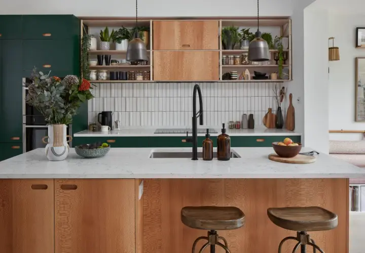 A modern kitchen island with wood grain cabinets and a white countertop, showcasing thoughtful kitchen styling with plants, fruit, and decorative items.