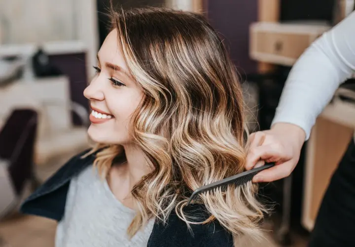 Sonrisa radiante con un balayage rubio natural, el cabello ondulado y con mechas doradas resalta su belleza.